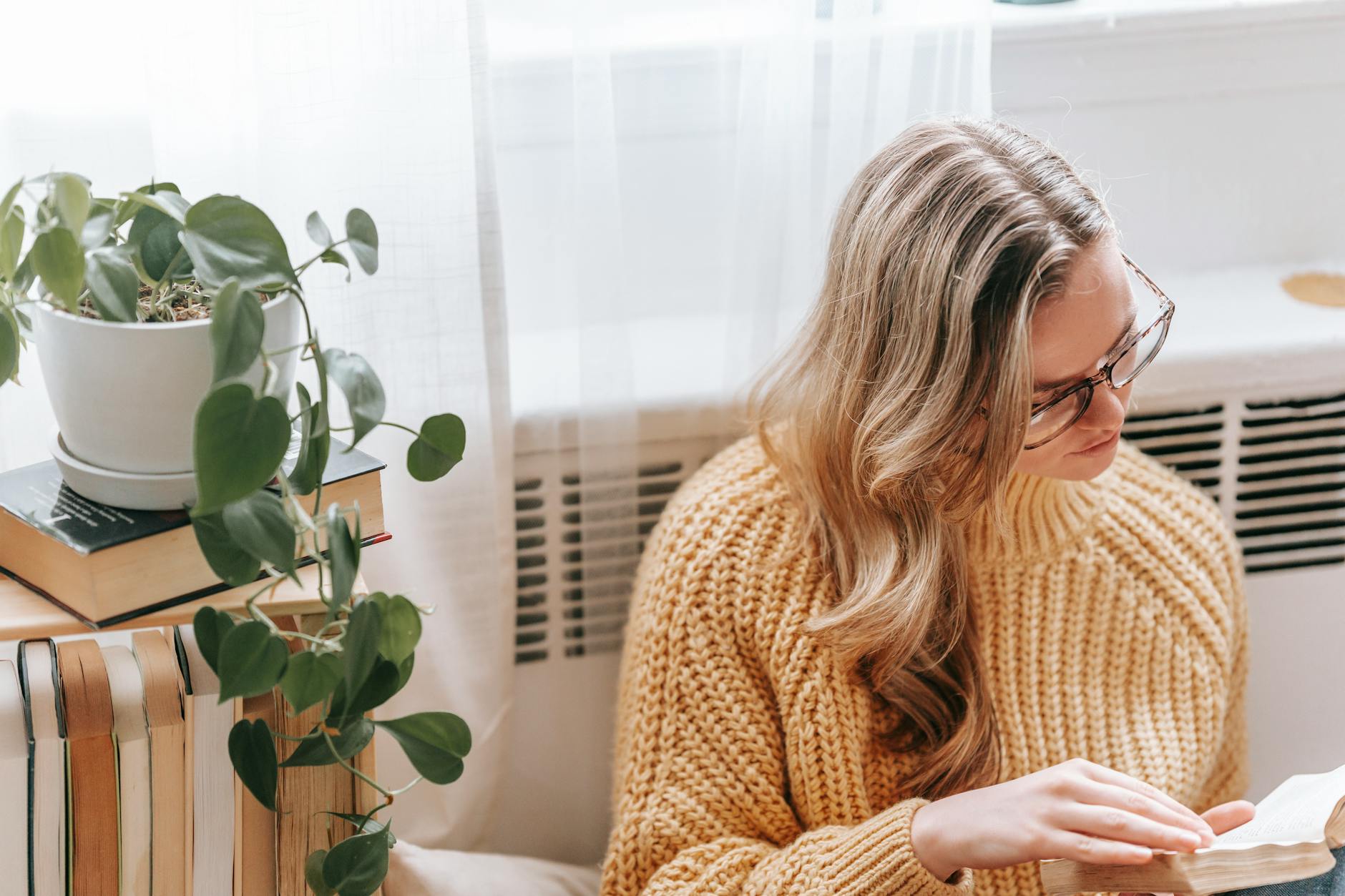 A young woman sitting comfortably in a light-filled room, reading a book — conveying focus, calm, and the inner life of an adult navigating daily challenges